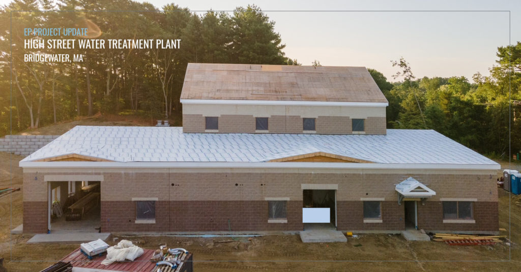 Building under construction sits in front of trees in sunlight.